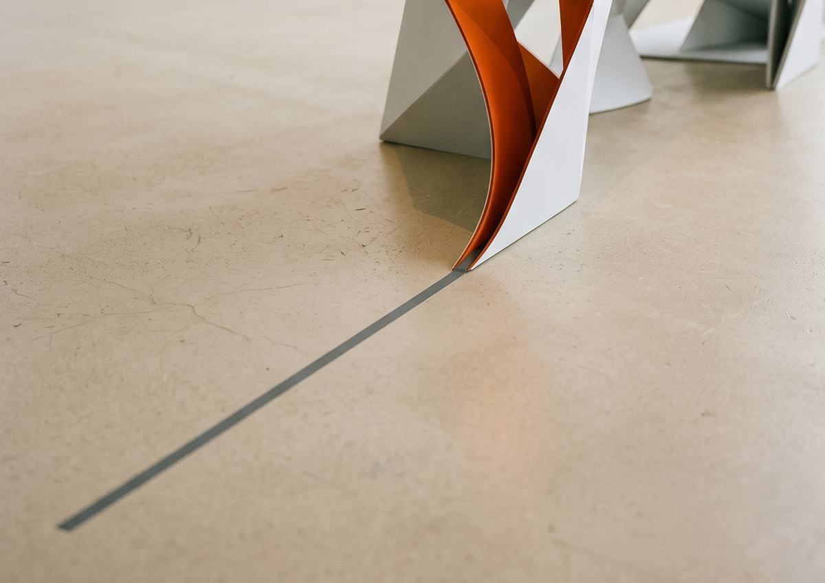 Fita de papel laranja saindo de uma escultura branca sobre piso de concreto, como um caminho que se abre